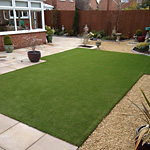 Artificial grass lawn surrounded by paving and gravel